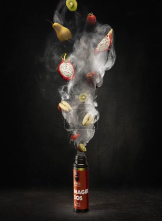 Téléchargez les photos : Liquide pour le ravitaillement d'une vape avec de la fumée debout sur une table en bois sombre et poire, kiwi, pomme, fraise et fruit du dragon volent dedans - en image libre de droit