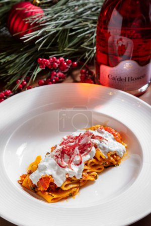 Téléchargez les photos : Pâtes aux crabes et crème sure dans une assiette sur la table avec une bouteille de vin et des décorations de Noël - en image libre de droit