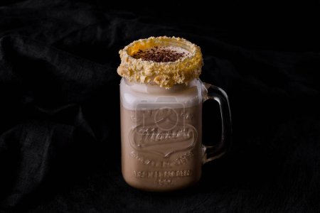 Photo for Coffee with frothy chocolate crumbs, and nuts in a glass that stands on a wooden table on a dark fabric background - Royalty Free Image