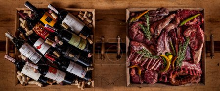 Photo for Different bottles of wine lying in a box with wine corks on the table and a box of different jerky, ribs, pepper, sausage, meat on the bone lying in a box - Royalty Free Image
