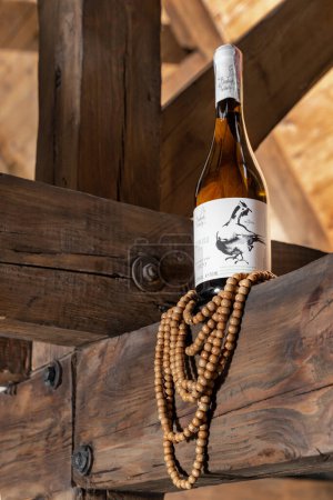 Foto de Una botella de vino seco blanco ucraniano Beykush se encuentra en vigas de madera, perlas de madera cuelgan de abajo. - Imagen libre de derechos