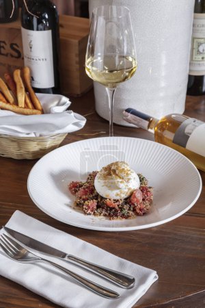Foto de Mozzarella with fish meat, sprouted seeds and parmesan in a plate with a glass of wine, cutlery, a bottle of wine and grissini in a basket standing on the table - Imagen libre de derechos