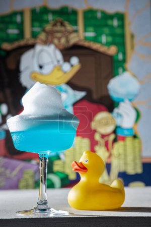 Téléchargez les photos : Cocktail bleu avec glace et dans un verre qui se tient sur la table avec un canard en plastique et un canard dessiné sur le fond - en image libre de droit