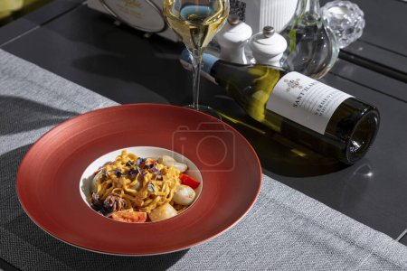 Téléchargez les photos : Spaghetti with squid, octopus, sprouts, tomatoes, cheese and sauce in a plate on the table with a glass of wine, a bottle of wine, pepper and salt - en image libre de droit