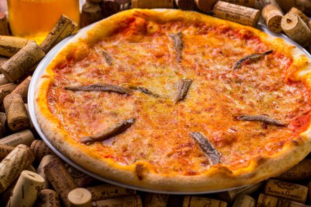 Téléchargez les photos : Pizza au fromage et poisson sur une assiette posée sur un ensemble de bouchons de vin avec des stands de vin - en image libre de droit