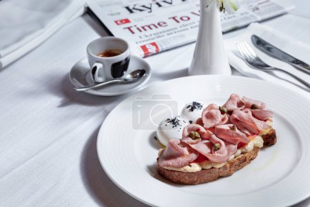 Foto de Sandwich con carne, garbanzos, salsa y huevos cocidos en un plato con cubiertos, una taza de café y un jarrón con flores sobre la mesa - Imagen libre de derechos