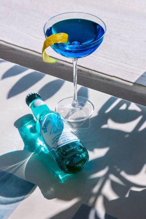 Photo for Blue cocktail with orange peel in a glass which stands on the table with a bottle of drink - Royalty Free Image