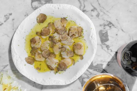 Photo for Scallop carpaccio with truffle mushroom slices in olive oil and herbs. Nearby is a glass of ros sparkling wine and a bottle of sparkling wine. - Royalty Free Image