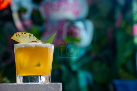 Téléchargez les photos : Cocktail avec glace, ananas séché, mousse et une feuille dans un verre au bord de la table - en image libre de droit