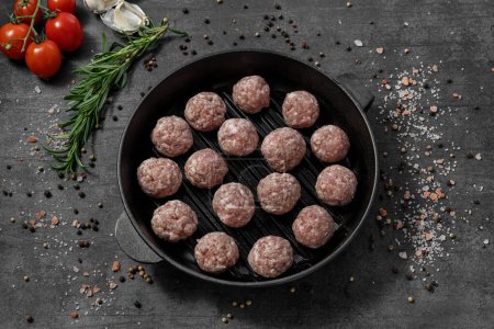 Photo for Veal meatballs. They lie on a black cast iron pan. The dishes stand on a dark stone background, spices and herbs are scattered around. - Royalty Free Image