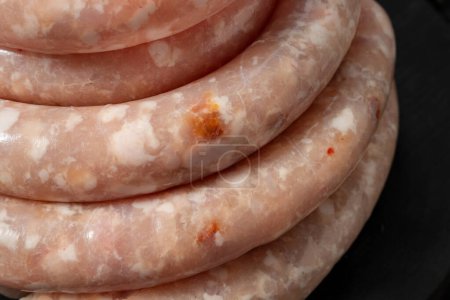 Photo for Chicken sausages with paprika and cheese. They lie on a black, wooden, round board. The dishes stand on a dark stone background, spices and herbs are scattered around. - Royalty Free Image