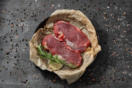 Photo for Veal tenderloin on parchment in a cast iron pan. The dishes stand on a dark stone background, spices and herbs are scattered around. - Royalty Free Image