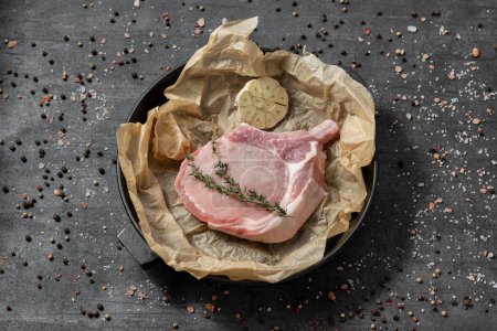 Photo for Pork on the bone on parchment in a cast iron pan. The dishes stand on a dark stone background, spices and herbs are scattered around. - Royalty Free Image