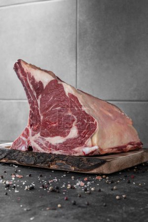 Photo for A piece of aged beef on a light wooden board, standing on a dark stone background, with salt and pepper mixed with peas scattered around. - Royalty Free Image