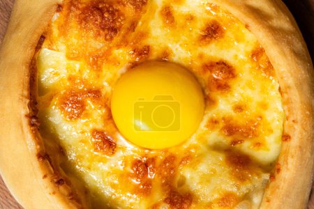 Photo for Boat-shaped Adjarian khachapuri with suluguni cheese and fresh yolk. Food lies on a wooden stand on a colored paper background. - Royalty Free Image