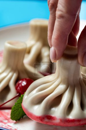Téléchargez les photos : Khinkali plat-dessert géorgien avec garniture cerise. Khinkali sont sur une assiette en céramique avec sauce cerise et feuilles de menthe. Placez la plaque sur un fond de papier coloré. - en image libre de droit