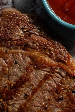 Téléchargez les photos : Le steak de porc repose sur du parchemin blanc sur une planche de bois. Un bol de sauce tomate et un brin de romarin sont à proximité.. - en image libre de droit