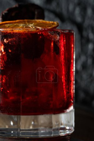 Téléchargez les photos : Cocktail avec mezcal et vermouth, liqueur et poire fumée, garni de frites d'orange dans un verre à l'ancienne. Tenez un verre avec un cocktail sur un tonneau en bois. - en image libre de droit