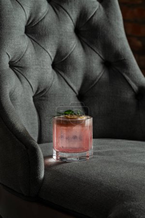 Photo for Cocktail with watermelon vodka, coconut liqueur, coconut milk and cocoa syrup in an old-fashioned glass. Stand the glass on a gray rag chair. - Royalty Free Image