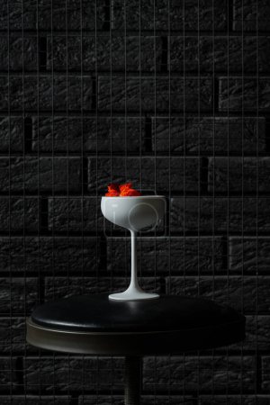 Photo for Cocktail with white gin and limoncello, soda and decorated with flowers. A cocktail in a white glass on a black bar stool. - Royalty Free Image