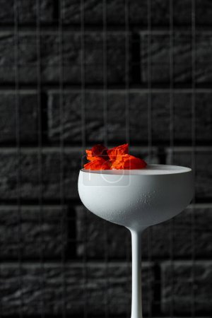 Photo for Cocktail with white gin and limoncello, soda and decorated with flowers. A cocktail in a white glass on a black bar stool. - Royalty Free Image