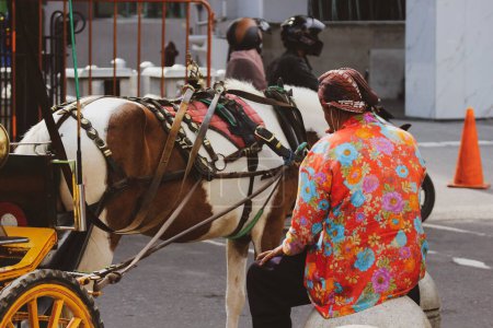 Téléchargez les photos : Vue arrière d'un wagon ou d'un chauffeur Andong sur Jalan Malioboro, Yogyakarta. Avec des vêtements de batik javanais typiques et des chapeaux blangkon. - en image libre de droit
