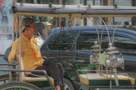 Téléchargez les photos : Yogyakarta en octobre 2022. Vue latérale d'un wagon ou d'un chauffeur Andong sur Jalan Malioboro, Yogyakarta. Avec des vêtements de batik javanais typiques et des chapeaux blangkon. Ils étaient assis sans réfléchir à attendre les passagers. - en image libre de droit