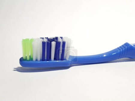Téléchargez les photos : Photo blanche isolée d'une brosse à dents en plastique qui a été utilisée plusieurs fois. Cette brosse à dents a une poignée bleue avec une brosse composée de vert, blanc et bleu. - en image libre de droit