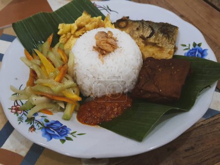 Photo for A portion of Nasi Kucing complete with fried milkfish head, tofu, served on a plate with banana leaves. On top of the rice sprinkled with fried onions to make it taste more delicious when eaten. - Royalty Free Image