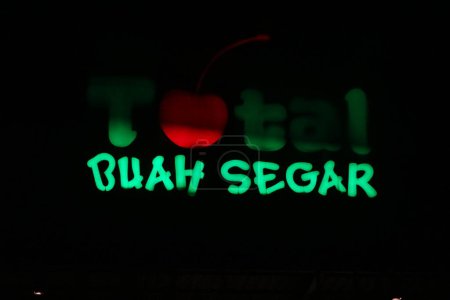 Téléchargez les photos : Bekasi, Indonesia in July 2022. The TOTAL Buah Segar logo shining brightly at night against the dark night sky. Total fresh fruit is a big fruit shop that is famous in Indonesia because it provides many types of fruit. - en image libre de droit