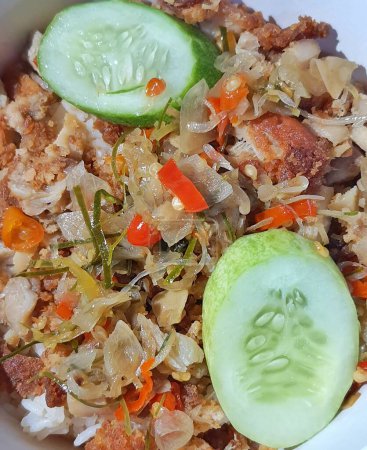 Foto de Close up photo of Ayam Geprek Sambal Matah, one of Indonesian specialties. Flour fried chicken is crushed and mixed with sambal matah. Served with rice and cucumber for lalapan. - Imagen libre de derechos
