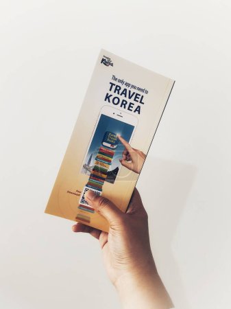 Téléchargez les photos : Jakarta, Indonesia in May 2022. A hand is holding a welcome guide book for travelers on vacation on Korea. The back page contains an advertisement for the KOREA TRAVEL BOOKS application. - en image libre de droit