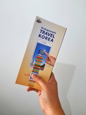 Téléchargez les photos : Jakarta, Indonesia in May 2022. A hand is holding a welcome guide book for travelers on vacation on Korea. The back page contains an advertisement for the KOREA TRAVEL BOOKS application. - en image libre de droit