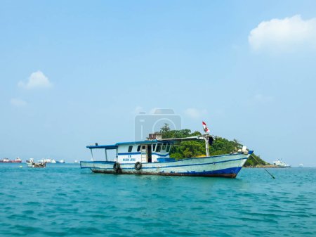 Téléchargez les photos : Une petite île dans le port de Merak, Cilegon, Banten. Vous pouvez voir la mer bleue, une petite île avec des arbres verts et un bateau de pêche autour. - en image libre de droit