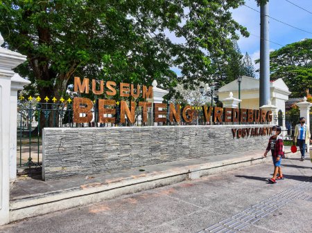 Téléchargez les photos : Yogyakarta, Indonésie en novembre 2022. Il est dit Musée Fort Vredeburg en brun, vous pouvez voir plusieurs visiteurs passant devant elle. Il s'agit d'un musée situé devant le bâtiment Agung et le palais du sultan. - en image libre de droit