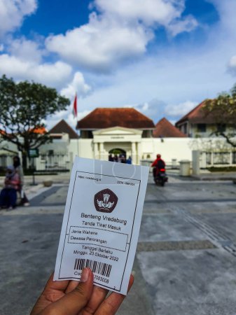 Téléchargez les photos : Yogyakarta, Indonesia in November 2022. A hand is holding a ticket to enter the Fort Vredeburg Museum, with the background behind it is the entrance to Fort Vredeburg. Previously this building served as one of the Dutch defense tools. There, the Dutc - en image libre de droit