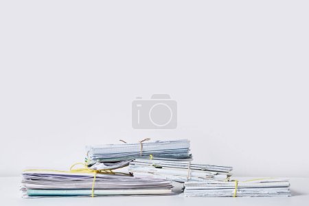 Foto de Varias pilas de papel sobre una superficie blanca con una cuerda amarilla atada a la parte superior e inferior, todas apiladas juntas - Imagen libre de derechos