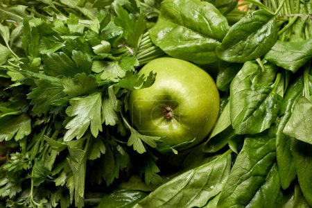 Photo for An apple and some green leaves on a cutting board in the background is a pile of chopped parsleys - Royalty Free Image