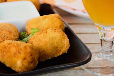 Photo for Croquettes or traditional Spanish homemade croquettes on a black plate with a beer on the side. Tapas food concept. - Royalty Free Image