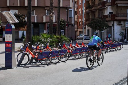 Photo for Viladecans - May 25 2023: Several parked ambici which is the shared bicycle available in various municipalities of the Barcelona metropolitan area, 100 electric while a cyclist passes by on a - Royalty Free Image