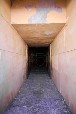 Téléchargez les photos : Couloir étroit avec un plafond bas qui mène à l'entrée d'une pyramide. Les murs et le plafond sont faits d'un plâtre orange-rose. Le sol est fait de tuiles de pierre grise - en image libre de droit