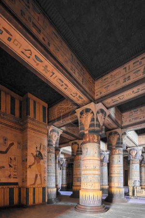 The Egyptian temple, with tall columns and intricate designs, houses sculptures of Hathor. The walls and ceiling are full of hieroglyphs. The photo shows an upward view of the dimly lit temple.