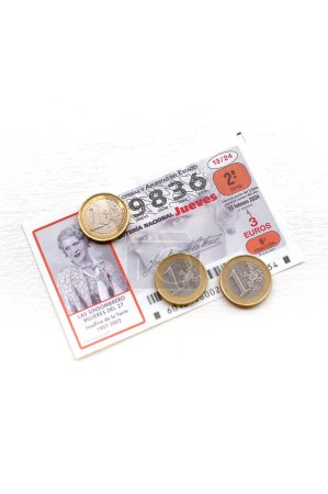 Foto de Barcelona, España - 16 de febrero de 2024: Billete de lotería nacional de España junto a tres monedas de euro sobre un fondo claro. - Imagen libre de derechos