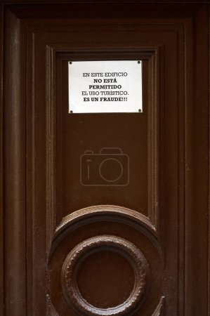 Téléchargez les photos : Image d'un panneau d'avertissement collé sur une porte brune indiquant l'interdiction d'utilisation touristique du bâtiment, l'appelant une fraude. Traduction : L'utilisation touristique n'est pas autorisée dans ce bâtiment, c'est une fraude - en image libre de droit