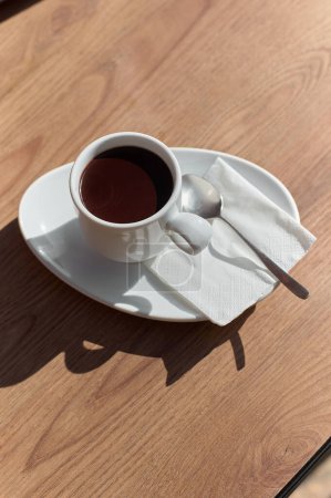 Tasse Schokolade auf einem Holztisch, beleuchtet von Sonnenlicht, das einen künstlerischen Schatten erzeugt.