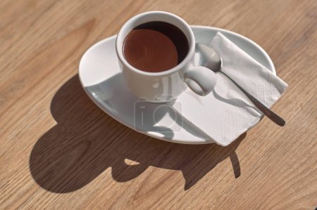 Tasse Schokolade auf einem Holztisch, beleuchtet von Sonnenlicht, das einen künstlerischen Schatten erzeugt.