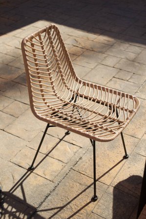 Vom Sonnenlicht beleuchteter Stuhl aus Rattan, der sein elegantes und handwerkliches Design hervorhebt, ideal für moderne Innen- und Außenräume.