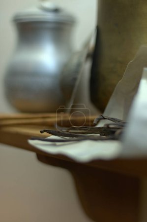 Téléchargez les photos : Gousses de vanille séchées reposant sur du papier blanc sur une étagère en bois, avec des vases hors foyer en arrière-plan. - en image libre de droit