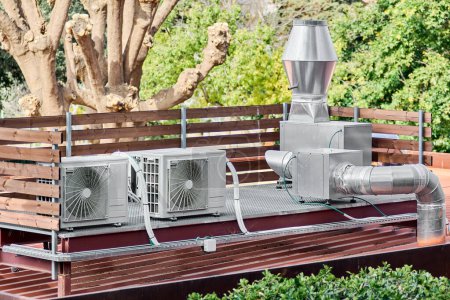 Téléchargez les photos : Système de climatisation extérieure sur un toit avec végétation autour, montrant l'intégration de la technologie et de la nature. - en image libre de droit