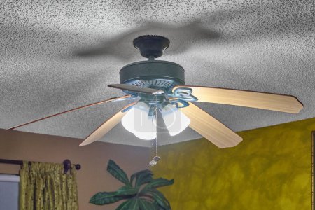 Ceiling fan with lights in living room, yellow wall and decorative plant.